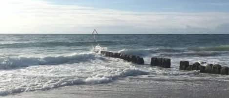 A beach with waves, a wooden jetty, and a clear sky.