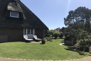 A thatched-roof house with a lawn and outdoor seating area. - Holiday home with 3 bedrooms (Wenningstedt-Braderup)