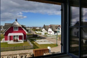 Ein rotes Haus mit weißer Veranda und einem Strohdach, umgeben von einer gepflasterten Fläche und weiteren Häusern.