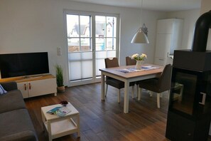 Ein modernes Wohnzimmer mit Flachbildfernseher, Esstisch mit Stühlen, einer Couch, einem kleinen Couchtisch und einer Zimmerpflanze.