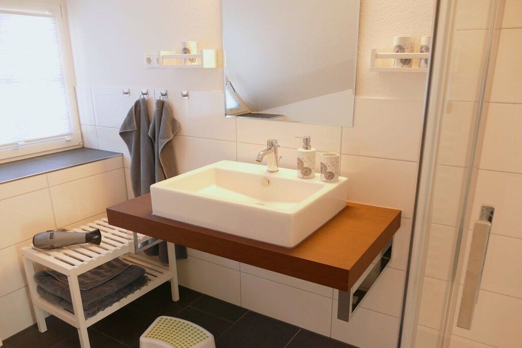 Ein Badezimmer mit einem weißen Waschbecken, einem Handtuchhalter, einem kleinen Hocker und einer Duschkabine.