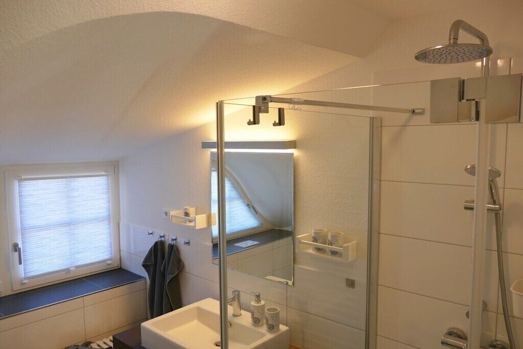Ein modernes Badezimmer mit einer gläsernen Duschkabine, einem Waschbecken und einem Fenster mit Jalousien.