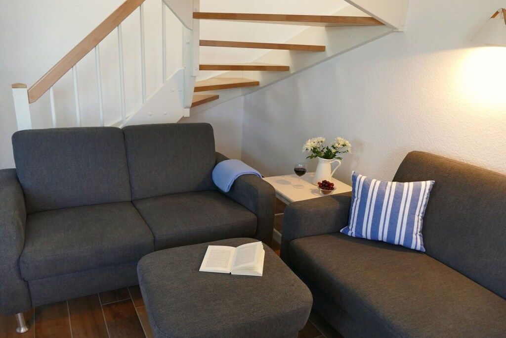 Un salon moderne avec un canapé gris, une petite table sur laquelle est posé un vase de fleurs et un livre sur un pouf.