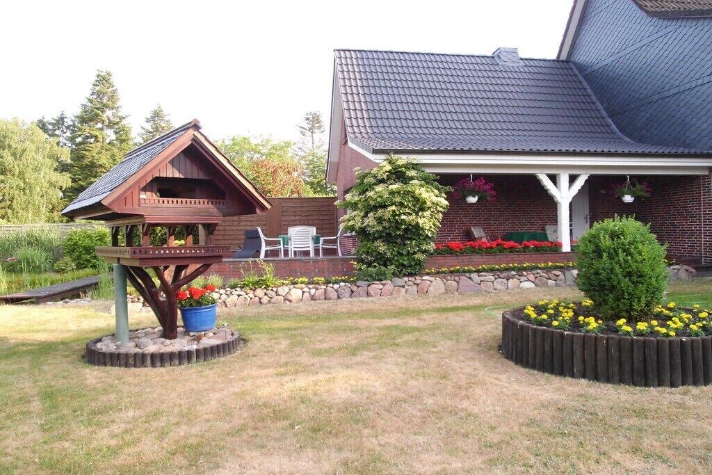 A house with a covered porch, a wooden deck, and a garden with flowers and shrubs.