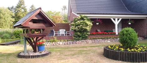 A house with a covered porch, a wooden deck, and a garden with flowers and shrubs.
