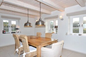 Ein Essbereich mit einem Holztisch, Korbstühlen, zwei Pendelleuchten und Fenstern mit weißen Rahmen.
