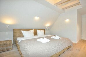 A bedroom with a large bed, two wall-mounted lights, a bedside table, and a wicker bench. - Holiday home with 3 bedrooms (Sankt Peter Ording)