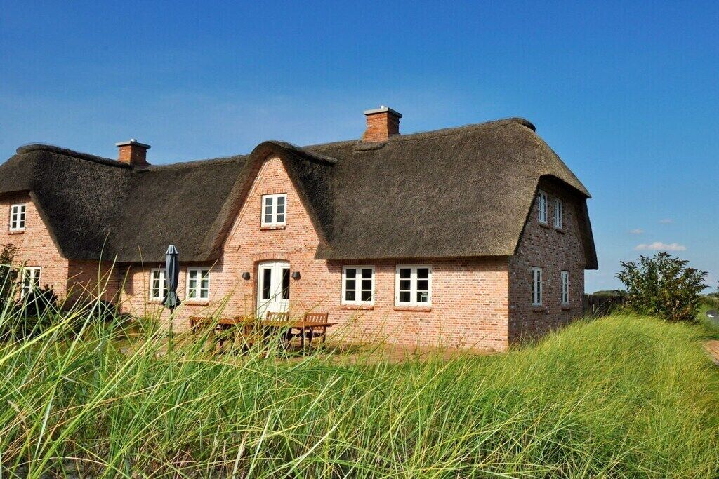 A traditional brick house with a thatched roof, a wooden door, and a bench outside.
