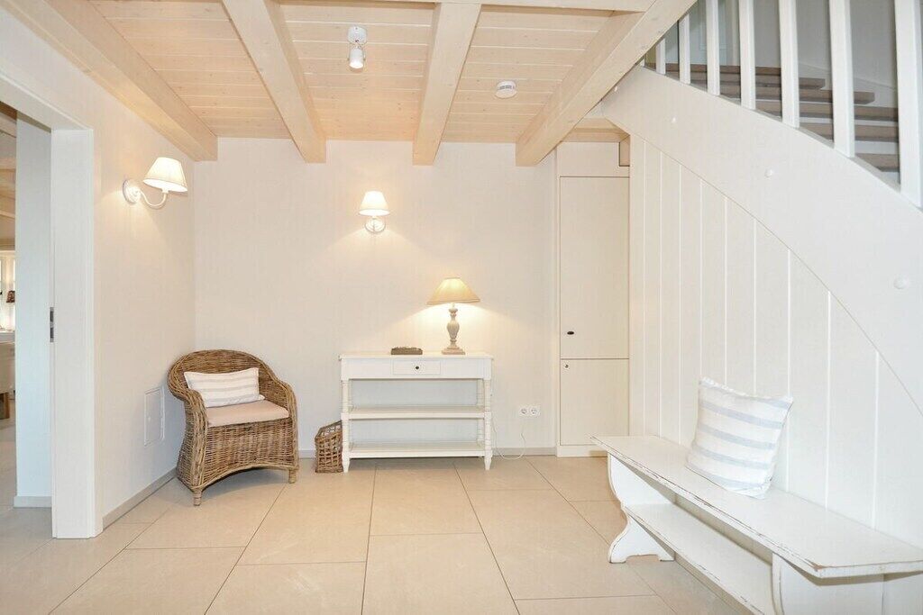 Quarto com um banco branco, uma cadeira de vime, uma mesinha de console branca com abajur e uma escada com corrimãos brancos.
