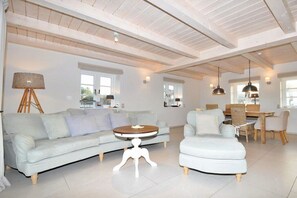 A spacious living area with a light-colored sofa, a round coffee table, and a dining table with chairs. - Holiday home with 3 bedrooms (Sankt Peter Ording)