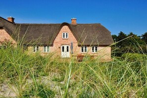 A traditional brick house with a thatched roof, surrounded by tall grass. - Holiday home with 3 bedrooms (Sankt Peter Ording)