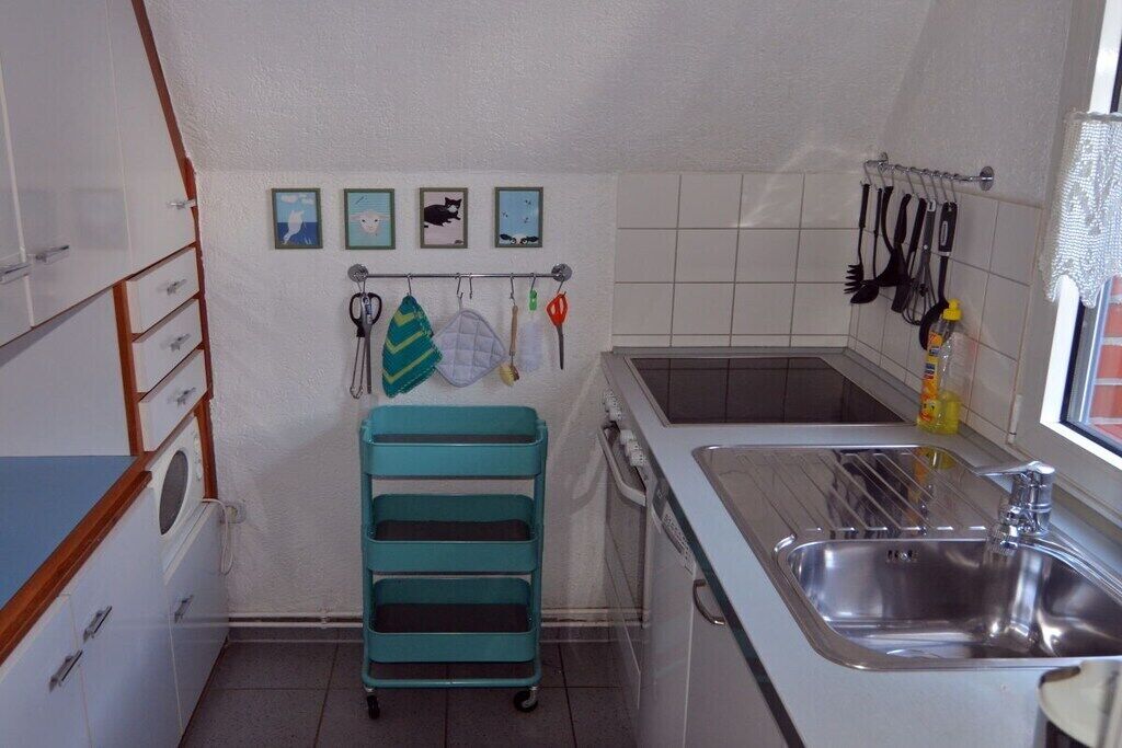 A kitchen with a sink, cabinets, a teal cart, and wall-mounted utensils.