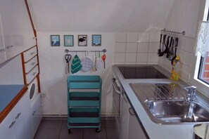 Eine Küche mit Spüle, Schränken, einem türkisblauen Wagen und an der Wand befestigten Küchenutensilien.