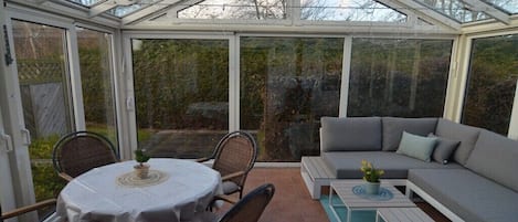 A conservatory with a dining table and chairs, a sofa, and a small table with a plant.