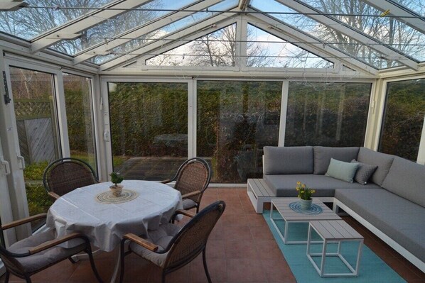 Ein Wintergarten mit Esstisch und Stühlen, einem Sofa und einem kleinen Tisch mit einer Pflanze.