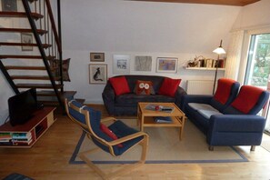 A living room with a sofa, two armchairs, a coffee table, a TV on a stand, a bookshelf, and a staircase. - Holiday home Wolkenblick (Wittmund - Harlesiel)