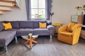A modern living room with a sectional sofa, a glass coffee table, a yellow armchair, and a small wooden side table. - Thatched house "Melsa" (Zierow)