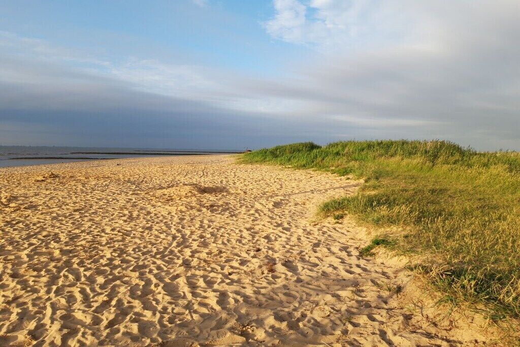 Une plage de sable fin, avec un ciel dégagé et un sentier qui mène à l’eau.