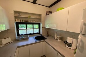 Una cocina moderna con armarios blancos, una ventana con cortinas de encaje, una cafetera y un tostador.