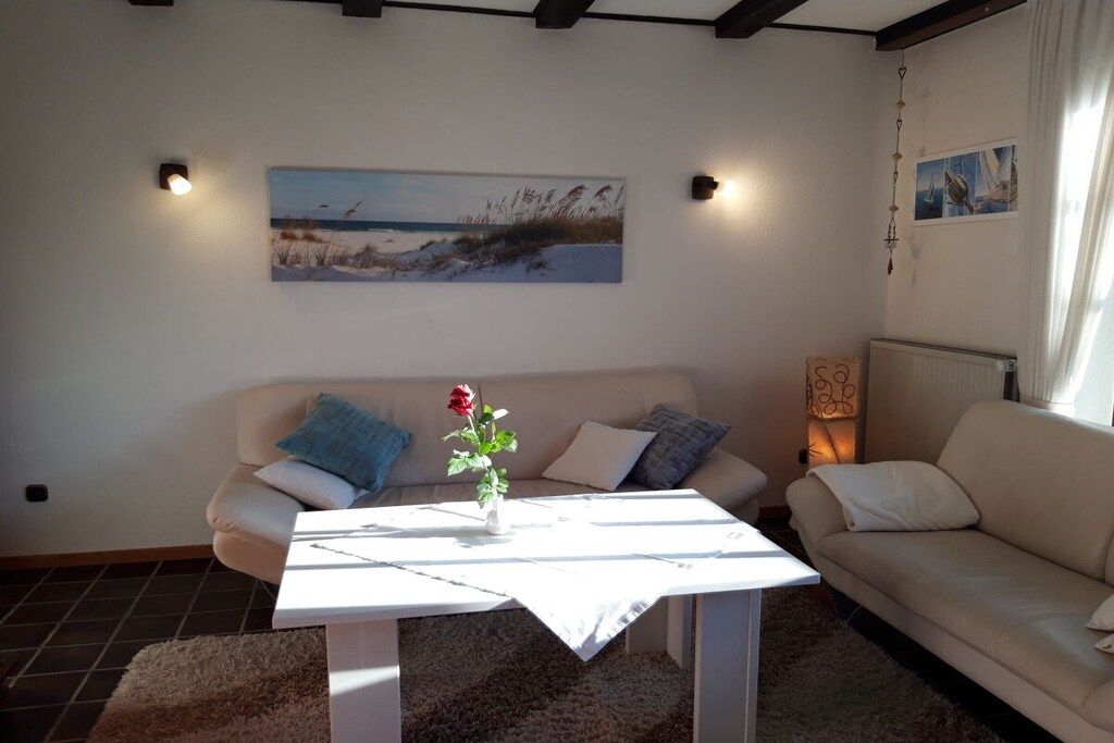 Een woonkamer met een witte bank, een bijzettafeltje met een bloevas, en een schilderij aan de muur.