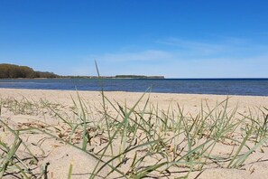 A beach with sand and grass in the foreground, a body of water in the middle ground, and a distant landmass on the horizon. - Thatched house "MOOI" (Zierow)
