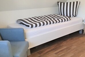 A single-bed room with a white mattress, striped pillows, and a blue chair. - Thatched house "MOOI" (Zierow)