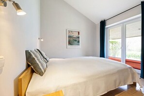 A bedroom with a bed, a nightstand, a wall-mounted lamp, and a window with curtains. - Holiday home in Bohnert with swimming pool (Bohnert)