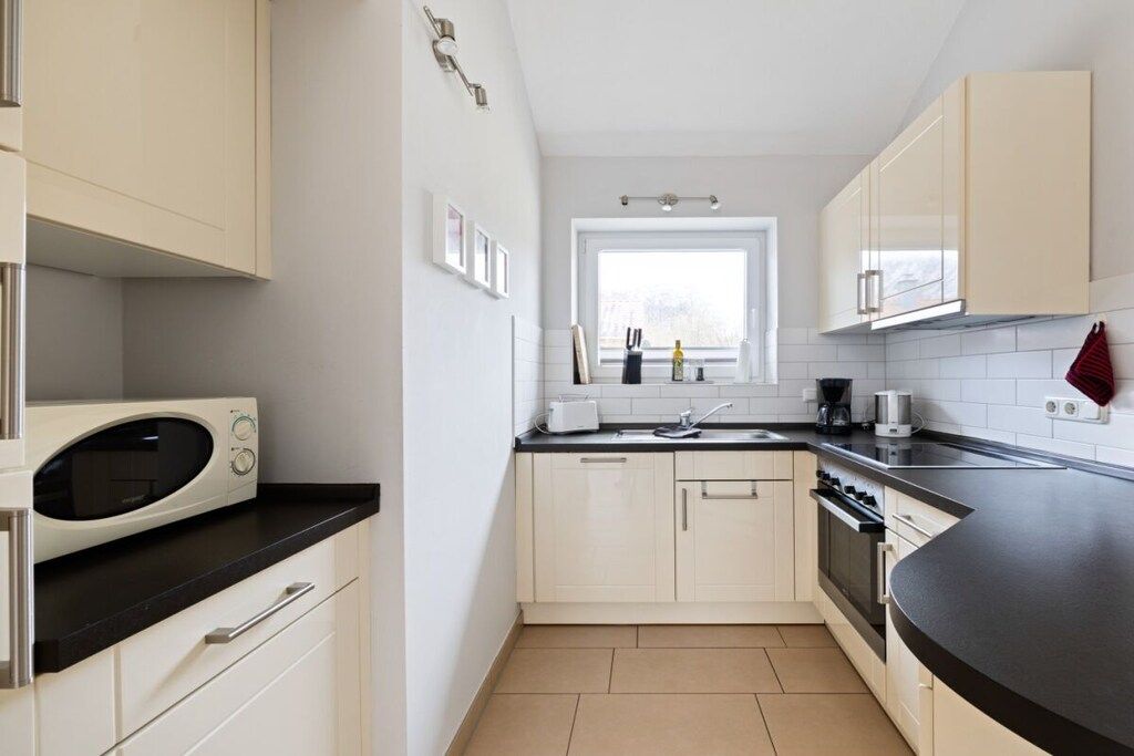 A modern kitchen with white cabinets, a black countertop, and a window providing natural light.