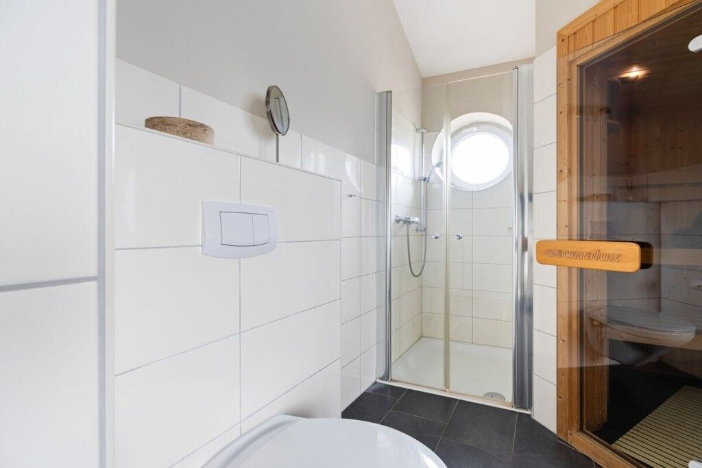 Un baño con ducha acristalada, inodoro blanco y zona de sauna de madera.