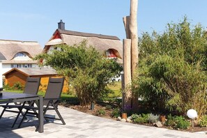 A thatched-roof building with a garden area featuring a table and chairs, surrounded by various plants and a wooden post. - Thatched house "Hemmer's Hus" (Zierow)