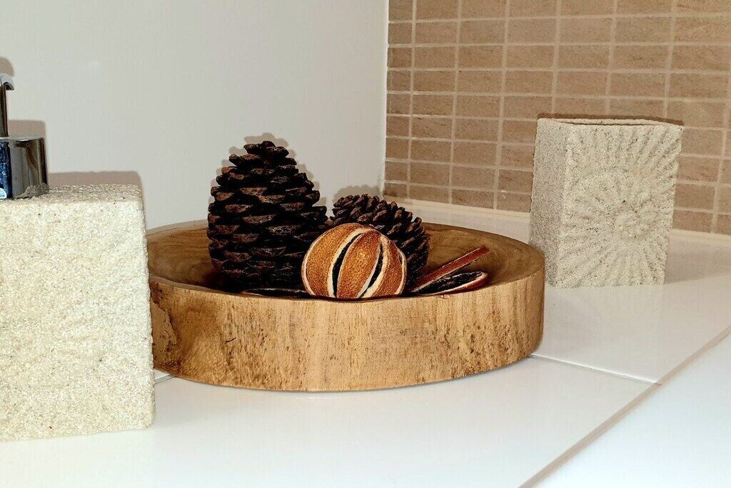 A wooden bowl containing pine cones and a decorative item on a white surface.