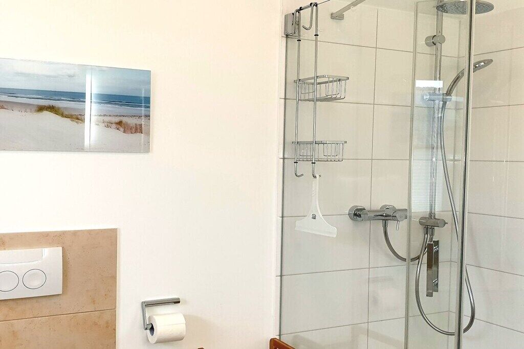 A bathroom with a glass-enclosed shower, a toilet paper holder, and a picture of a beach.