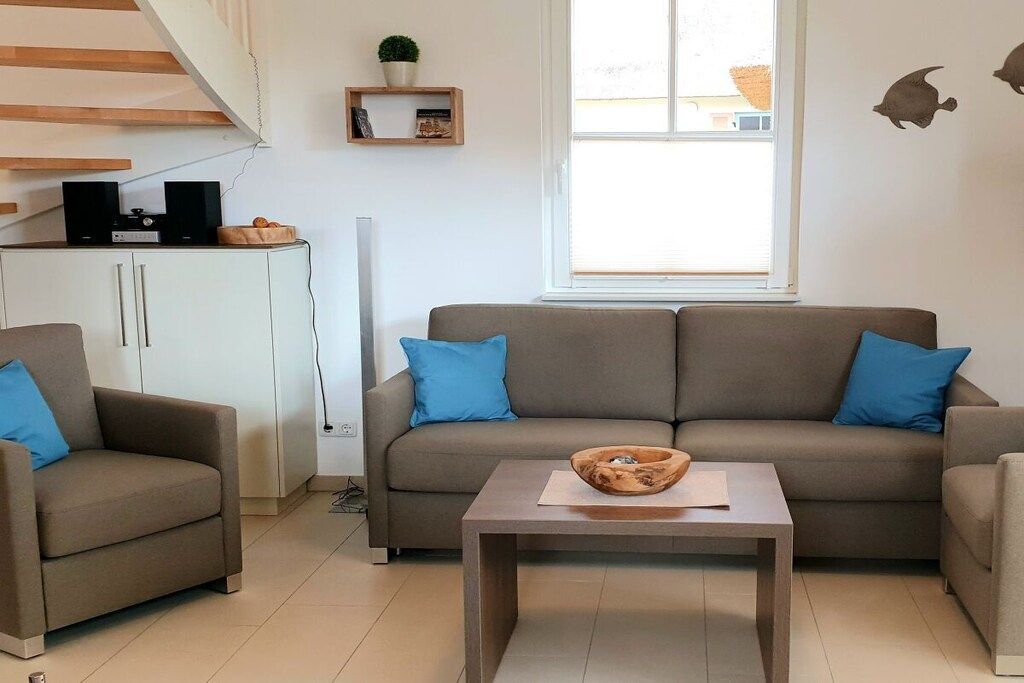 Een woonkamer met een bank, twee fauteuils, een salontafel, een witte kast en een raam met jaloezieën.