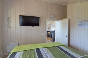 Habitació amb un llit, una televisió penjada a la paret i una porta que dona a una altra habitació.
