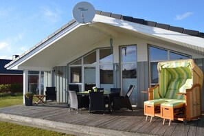 Een overdekt terras met een eettafel en stoelen, een lounge stoel en een schotelantenne.