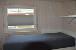 Una habitació amb finestra, un llit i una estant amb una làmpada.