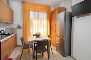 A compact kitchen with a dining table, chairs, a refrigerator, and a window with curtains. - Residence Marzia (Rivazzurra)