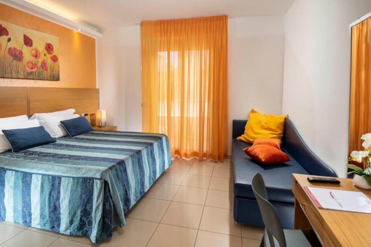 A hotel room with a bed, a sofa, a desk, and a painting on the wall.