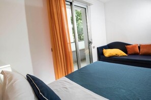 A hotel room with a bed, a sofa, a sliding glass door, and a curtain. - Residence Marzia (Rivazzurra)