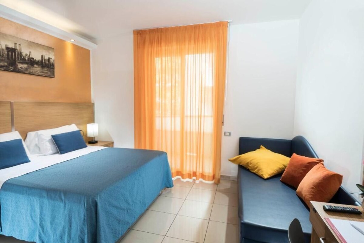 A hotel room with a bed, a sofa, a desk, and a window with curtains.