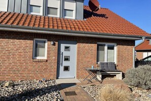 A brick house with a red-tiled roof, a satellite dish, and a small patio with a table and chair. - Holiday home in Zierow with swimming pool (Zierow)