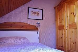 A bedroom with a wooden headboard, a bed with a patterned bedspread, a framed picture on the wall, and wooden wardrobe doors. - Holiday apartment on the Flensburg Fjord (Westerholz)