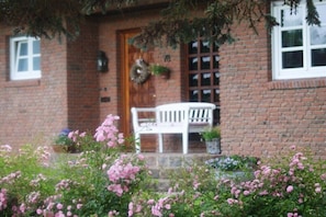 A brick building with a white bench in front, a door with a wreath, and a window with a grid pattern. - Holiday apartment on the Flensburg Fjord (Westerholz)