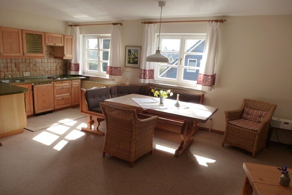 Une cuisine avec des meubles de rangement en bois, une table à manger avec des chaises et une fenêtre avec des rideaux.