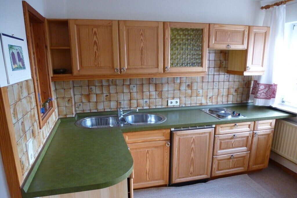 Een keuken met houten kastjes, een groen aanrecht, een spoelbak en een betegelde achterwand.