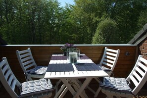 Ein Sitzbereich im Freien mit Tisch und Stühlen, umgeben von einer Holzterrasse und Bäumen.