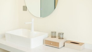 Un baño con un lavamanos blanco, un espejo redondo y dos pequeños recipientes en la encimera.