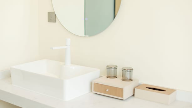 A bathroom with a white sink, a round mirror, and two small containers on the countertop.