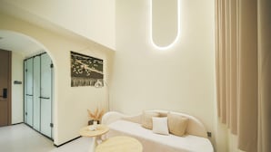 A modern living room with a white sofa, round wooden side tables, and a wall-mounted artwork.