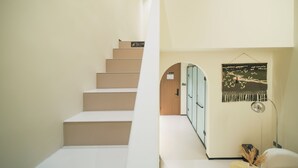 A staircase leading to a room with a door, a wall-mounted tapestry, and a lamp.
